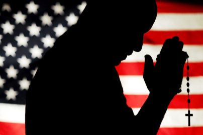 PHOTO ILLUSTRATION OF MAN HOLDING ROSARY WITH U.S. FLAG IN BACKGROUND