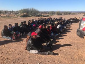 Large group of aliens sitting down after being apprehended near the US-Mexico border in Arizona