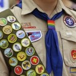 IMAGE VIA time.com - Merit badges and a rainbow-colored neckerchief slider are affixed on a Boy Scout uniform outside the headquarters of Amazon in Seattle. The U.S. organization, which now welcomes girls into the program and allows them to work toward the coveted Eagle Scout rank, announced Tuesday, May 7, 2024, that it will change its name to Scouting America as it focuses on inclusion. (AP Photo/Ted S. Warren, File)