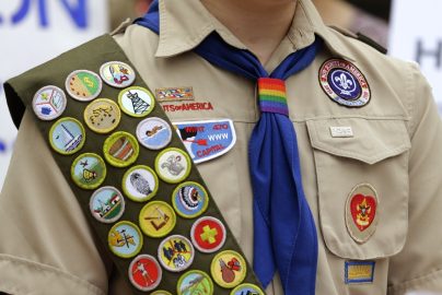 IMAGE VIA time.com - Merit badges and a rainbow-colored neckerchief slider are affixed on a Boy Scout uniform outside the headquarters of Amazon in Seattle. The U.S. organization, which now welcomes girls into the program and allows them to work toward the coveted Eagle Scout rank, announced Tuesday, May 7, 2024, that it will change its name to Scouting America as it focuses on inclusion. (AP Photo/Ted S. Warren, File)