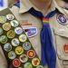 IMAGE VIA time.com - Merit badges and a rainbow-colored neckerchief slider are affixed on a Boy Scout uniform outside the headquarters of Amazon in Seattle. The U.S. organization, which now welcomes girls into the program and allows them to work toward the coveted Eagle Scout rank, announced Tuesday, May 7, 2024, that it will change its name to Scouting America as it focuses on inclusion. (AP Photo/Ted S. Warren, File)
